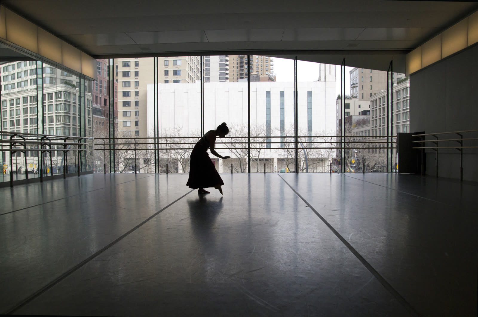 A dancer silhouetted against tall windows in an empty studio
